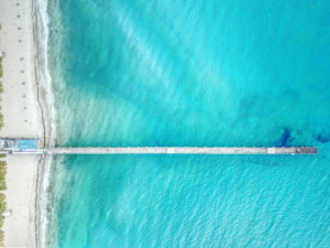 aerial-view-of-concrete-pier-and-turquoise-blue-sea-water-and-white-sandy-beach